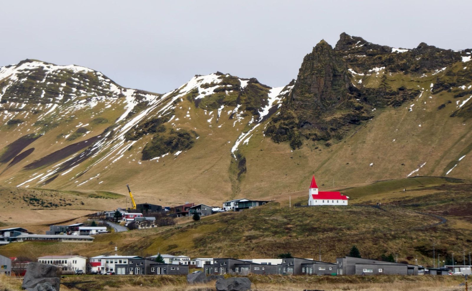 The village of Vík, Iceland, with a red-roofed church on a hill below snow-streaked green mountains